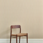 A wooden dining chair against a wallpaper playful hand drawn dotted stripe in soft yellow. 