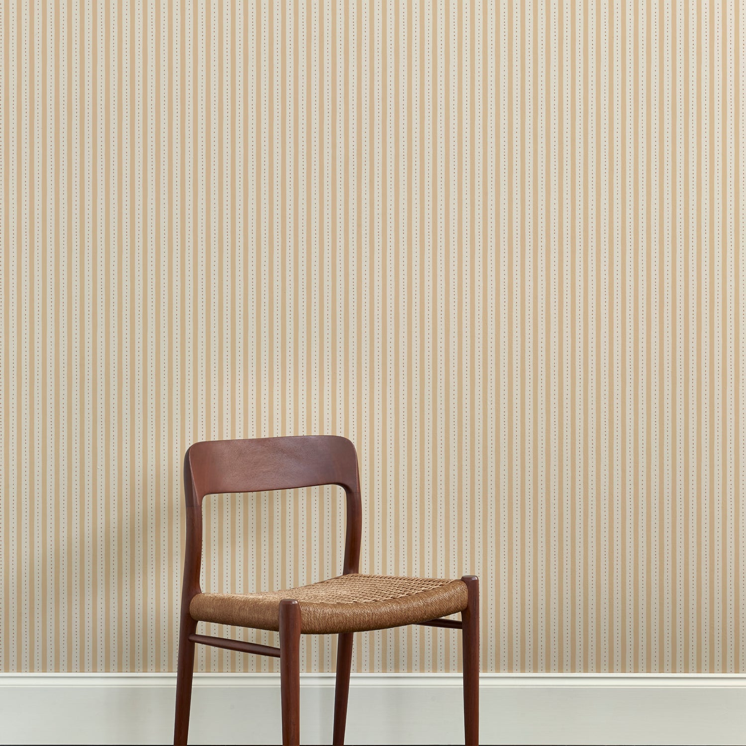 A wooden dining chair against a wallpaper playful hand drawn dotted stripe in soft yellow. 