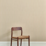 A wooden dining chair against a wallpaper playful hand drawn dotted stripe in soft yellow. 