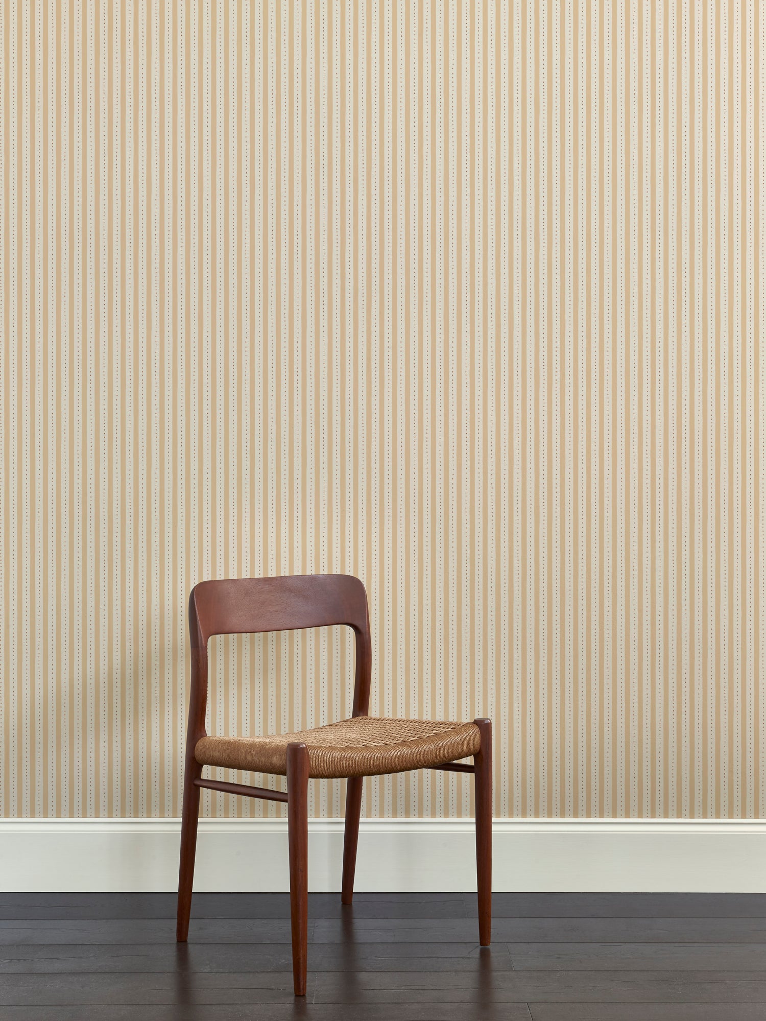 A wooden dining chair against a wallpaper playful hand drawn dotted stripe in soft yellow. 