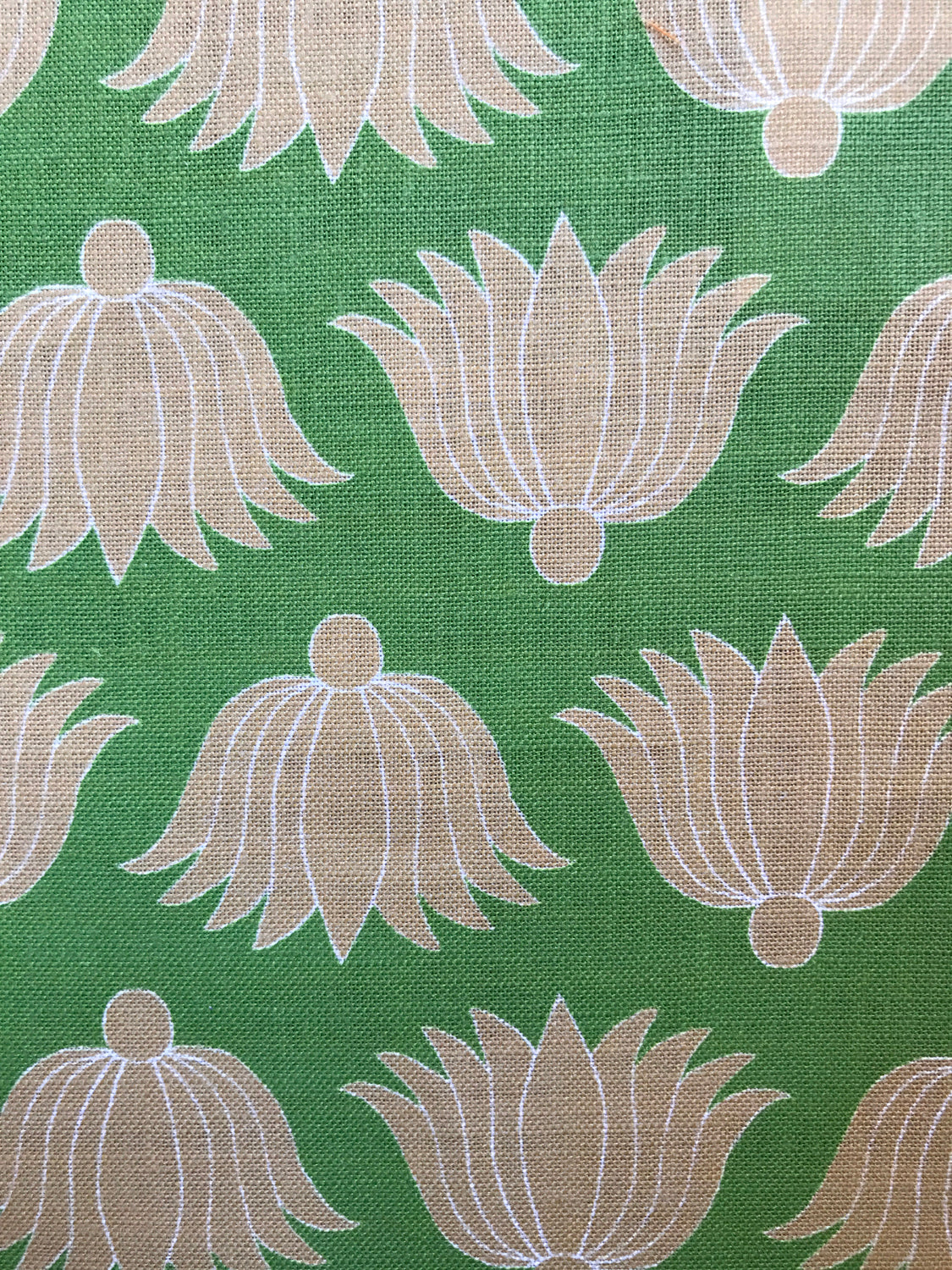 Detail of fabric in a repeating lotus print in tan and white on a green field.