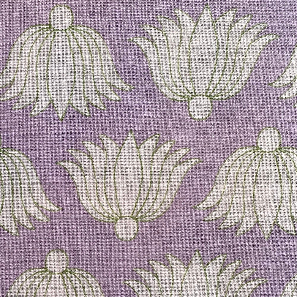 Detail of fabric in a repeating lotus print in cream and green on a purple field.