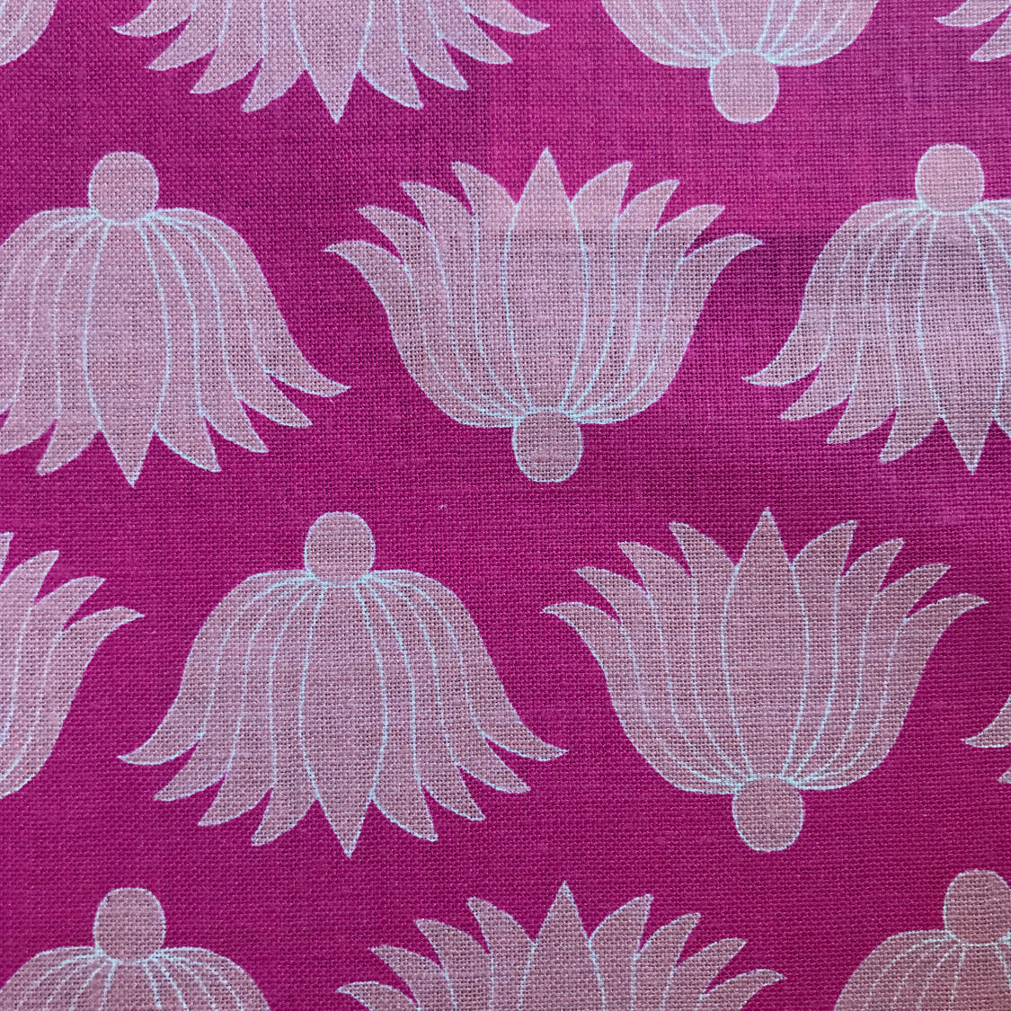 Detail of fabric in a repeating lotus print in light pink and white on a magenta field.