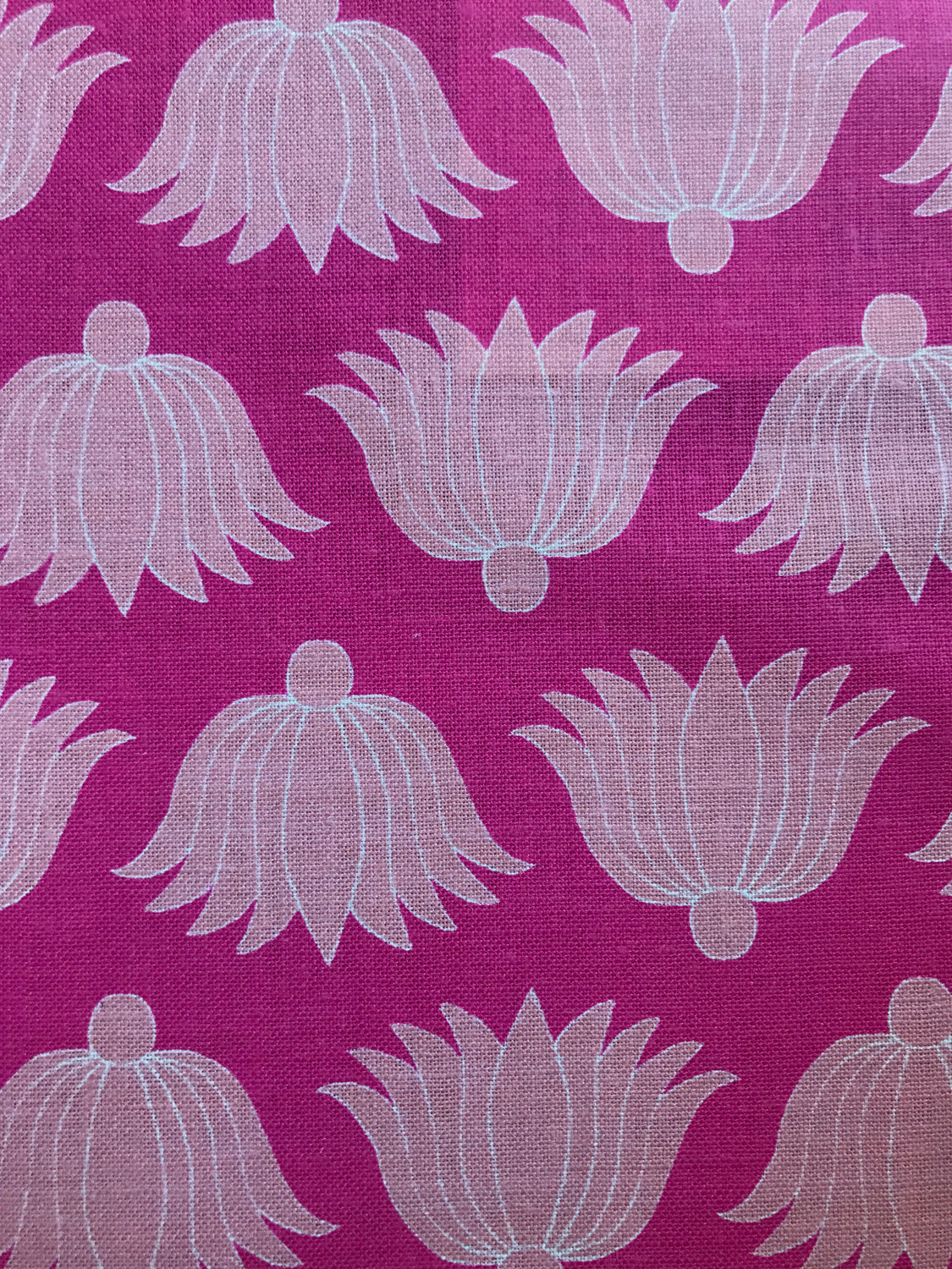 Detail of fabric in a repeating lotus print in light pink and white on a magenta field.