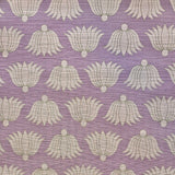 Detail of fabric in a repeating lotus print in cream and tan on a light purple field.