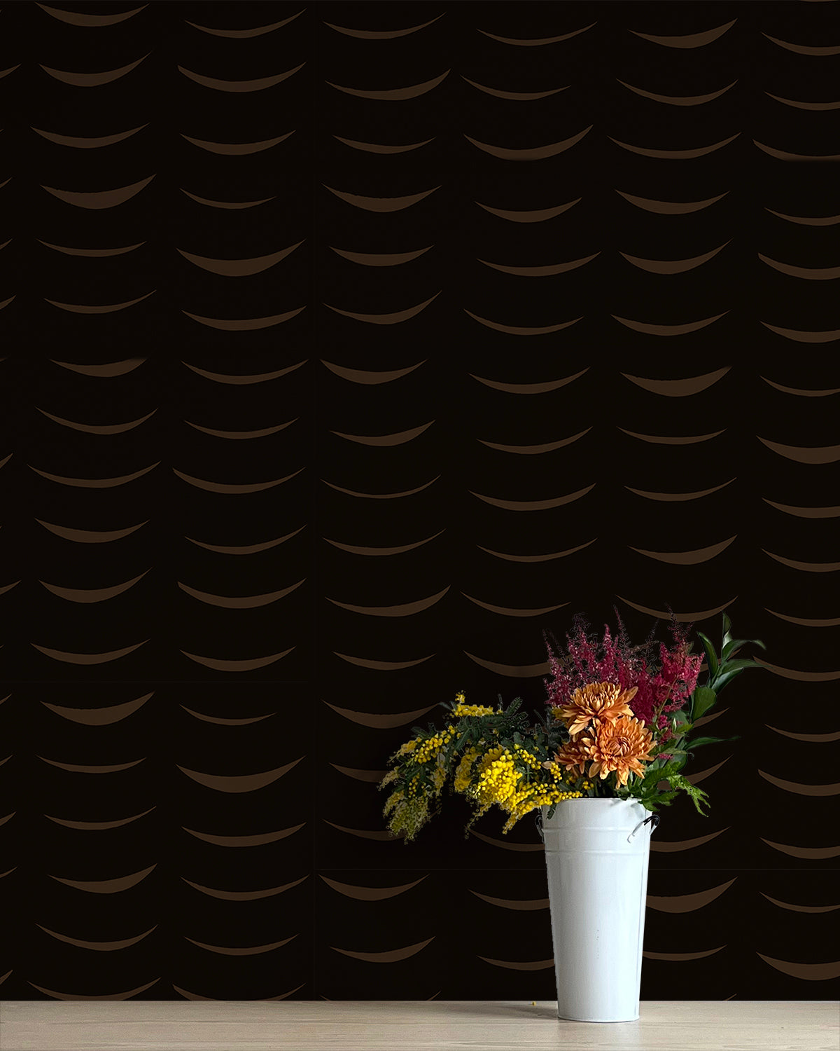 A vase of flowers stands in front of a wall papered in an abstract crescent print in brown on a black field.