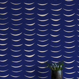 A vase of flowers stands in front of a wall papered in an abstract crescent print in cream on a navy field.