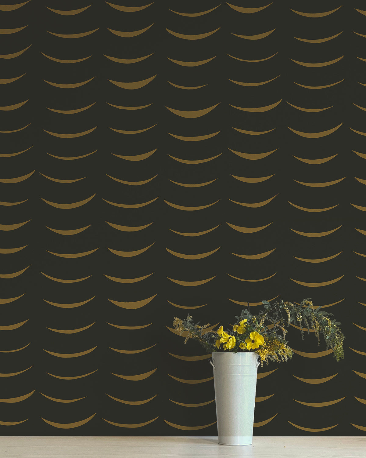 A vase of flowers stands in front of a wall papered in an abstract crescent print in brown on a black field.