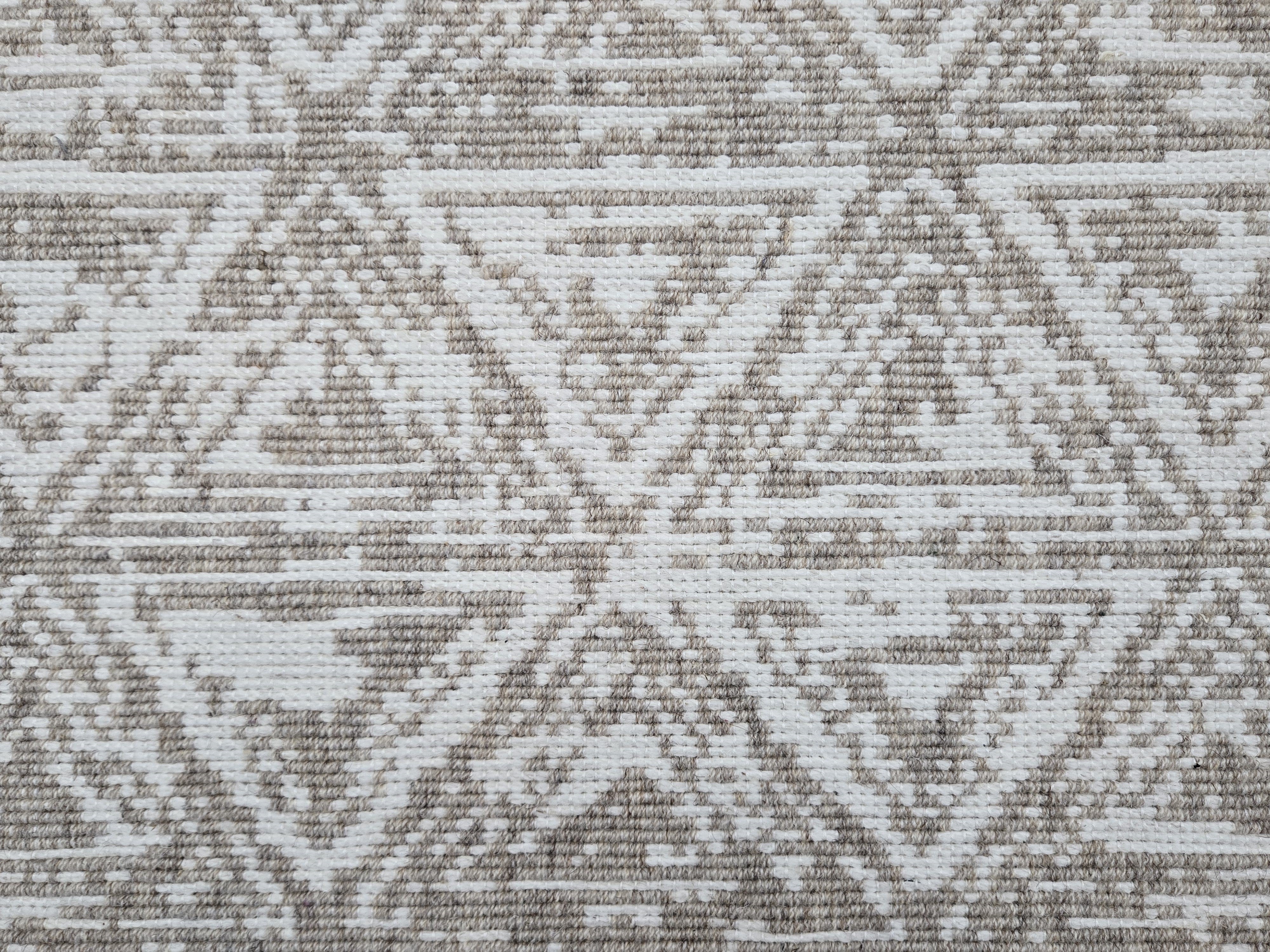 Broadloom carpet sample in a textural stacked triangle pattern in white and oatmeal.