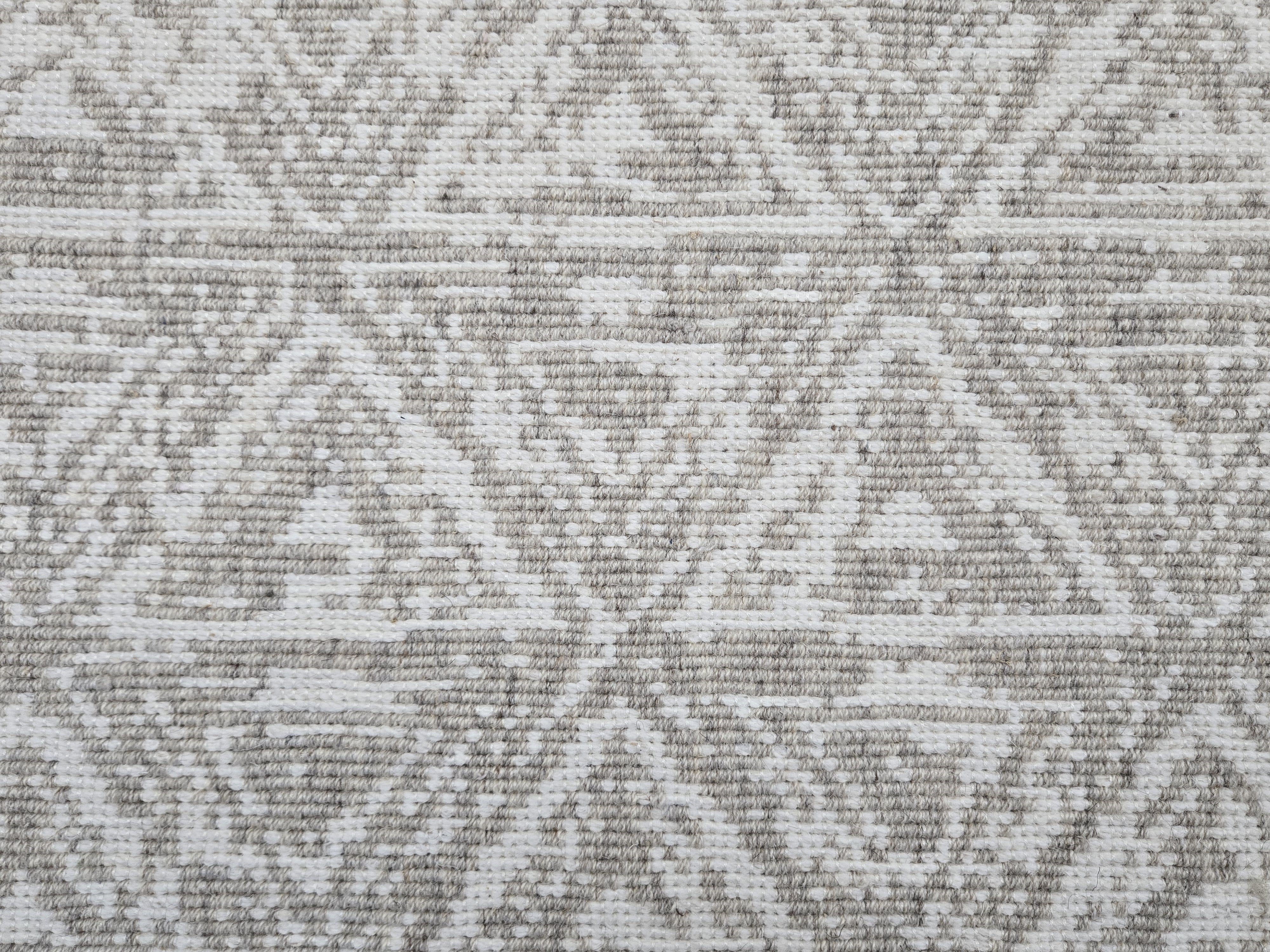 Broadloom carpet sample in a textural stacked triangle pattern in white and taupe.