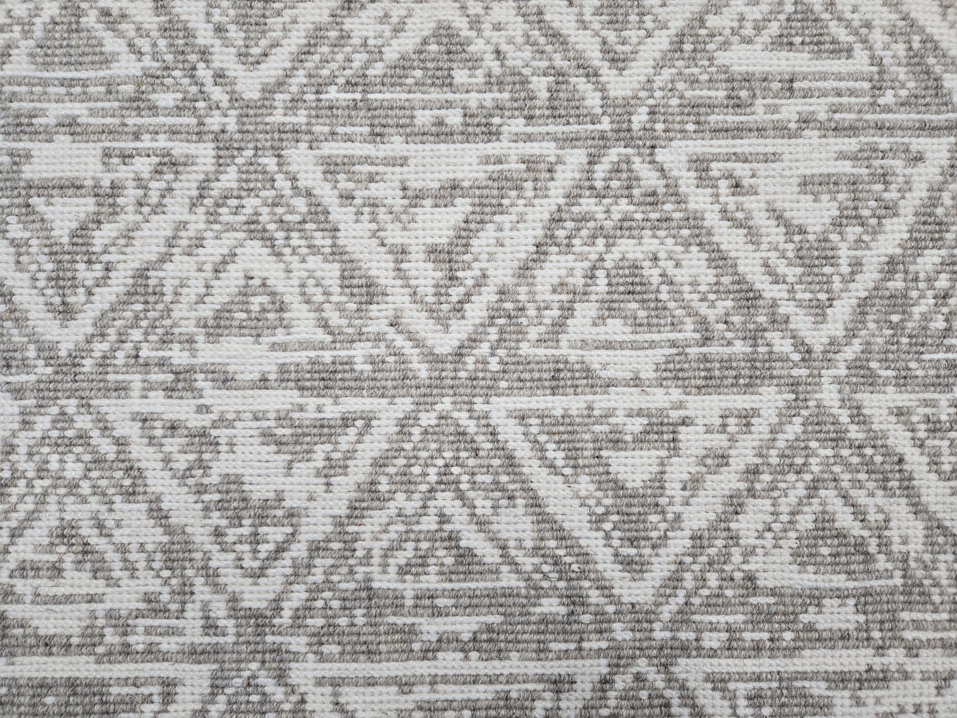 Broadloom carpet sample in a textural stacked triangle pattern in white and grey.