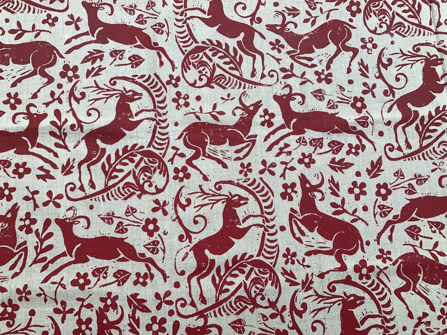 Detail of fabric in a deer, leaf and flower print in red on a white field.