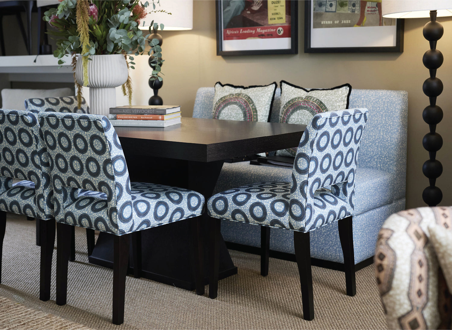 Dining room with patterned chairs around a wooden table, lamp, and framed pictures on the wall.