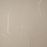 Detail of a wallpaper in an elongated paint splatter pattern in metallic gold on a cream field.