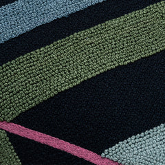 Detail of fabric with a large-scale geometric print embroidered in shades of blue, olive and pink on a dark navy field.