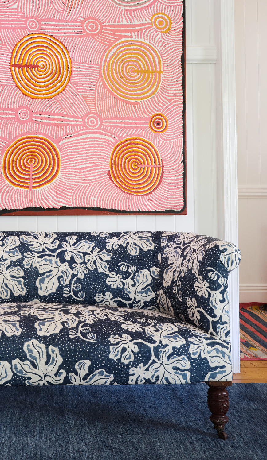 A couch upholstered in a playful botanical print in navy and white stands in front of a large-scale pink and orange painting.