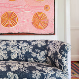 A couch upholstered in a playful botanical print in navy and white stands in front of a large-scale pink and orange painting.