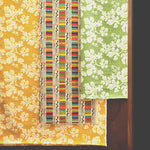 A wall draped in three different pieces of fabric yardage, two in painterly floral prints and one in a geometric grid print.