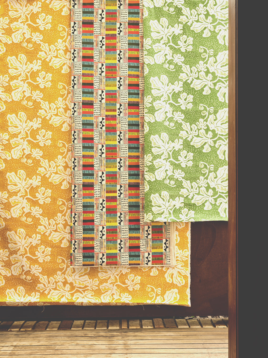 A wall draped in three different pieces of fabric yardage, two in painterly floral prints and one in a geometric grid print.