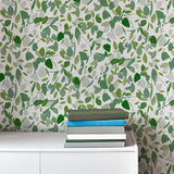 An end table and books stand in front of a wall papered in a minimal leaf print in shades of green, gray and white.
