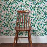 A wooden chair stands in front of a wall papered in a minimal leaf print in shades of green, pink and white.