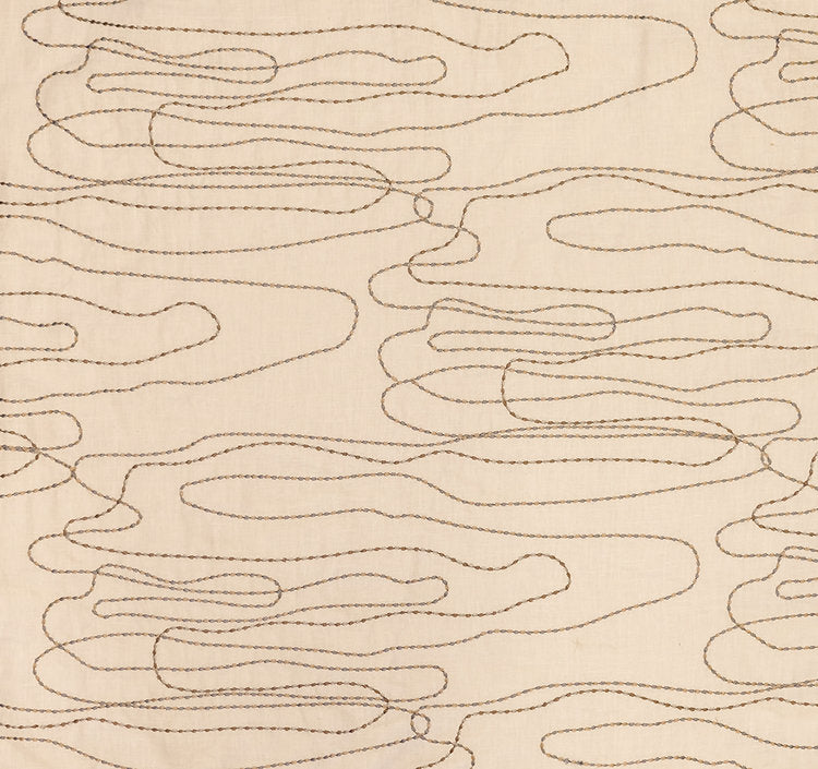 Detail of fabric in an abstract embroidered pattern in tan on a cream field.