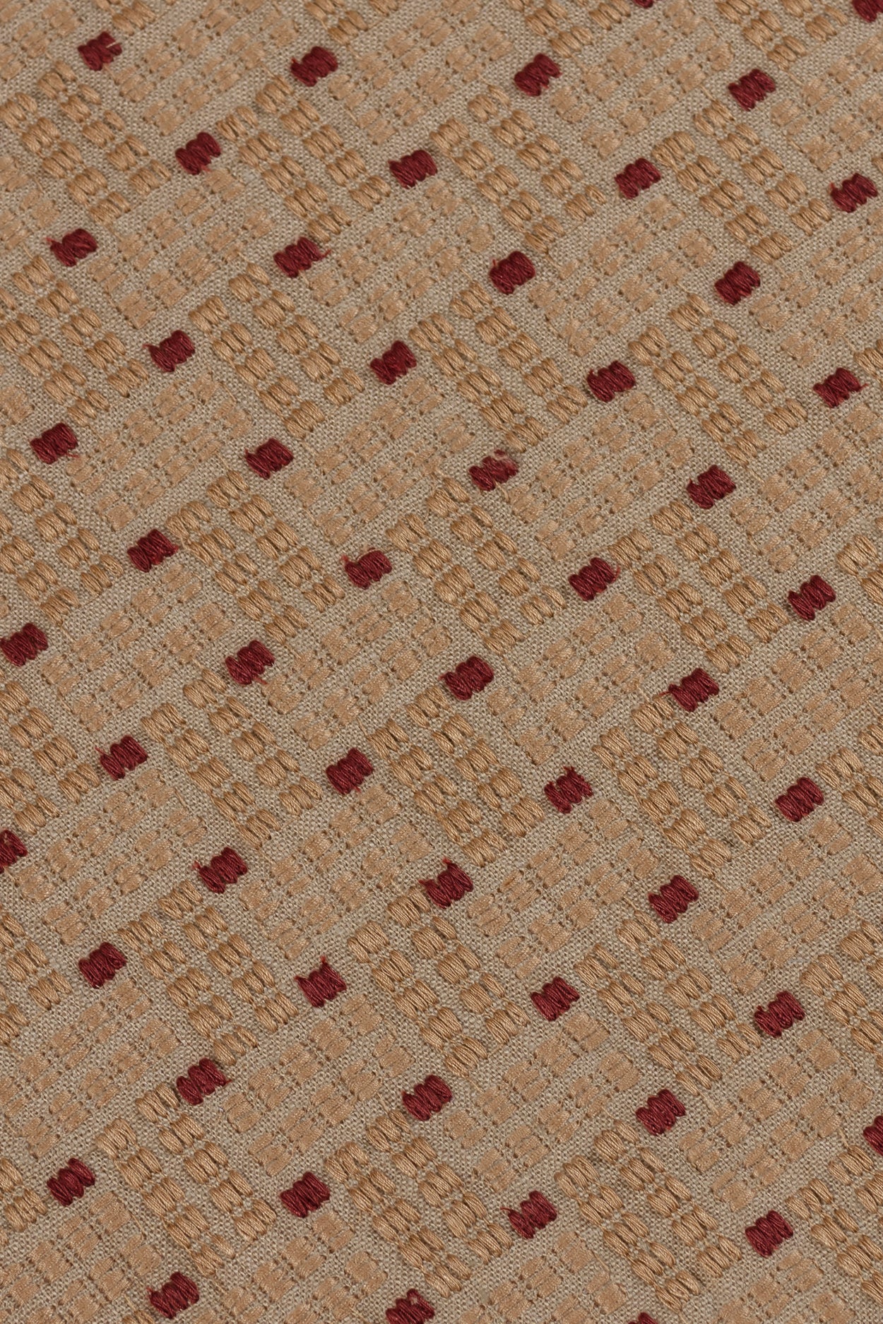 Detail of an embroidered fabric in a dashed basketweave design in tan with red accents.