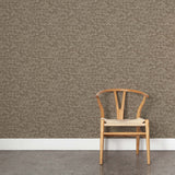 A wooden chair stands in front of a wall papered in a textural geometric print in shades of brown on a brown field.