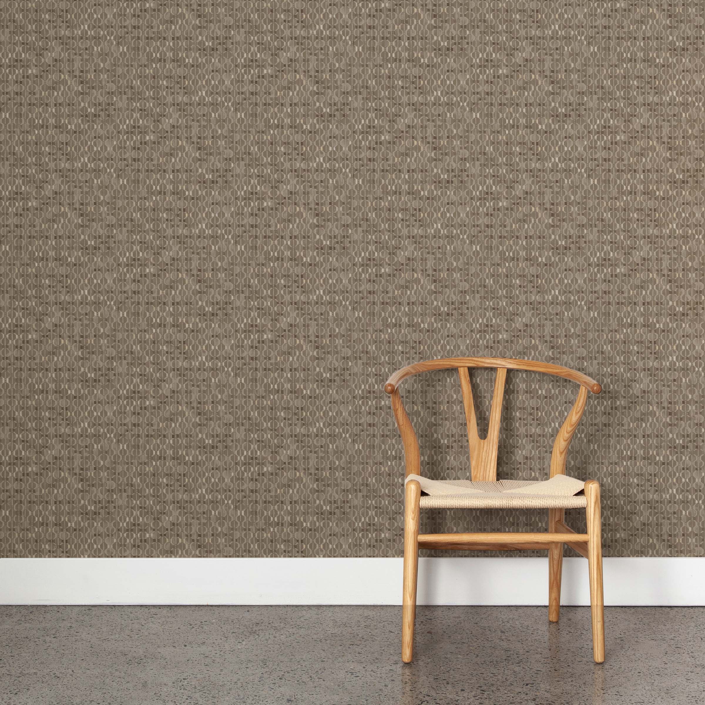 A wooden chair stands in front of a wall papered in a textural geometric print in shades of brown on a brown field.