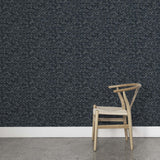 A wooden chair stands in front of a wall papered in a textural geometric print in shades of gray on a charcoal field.