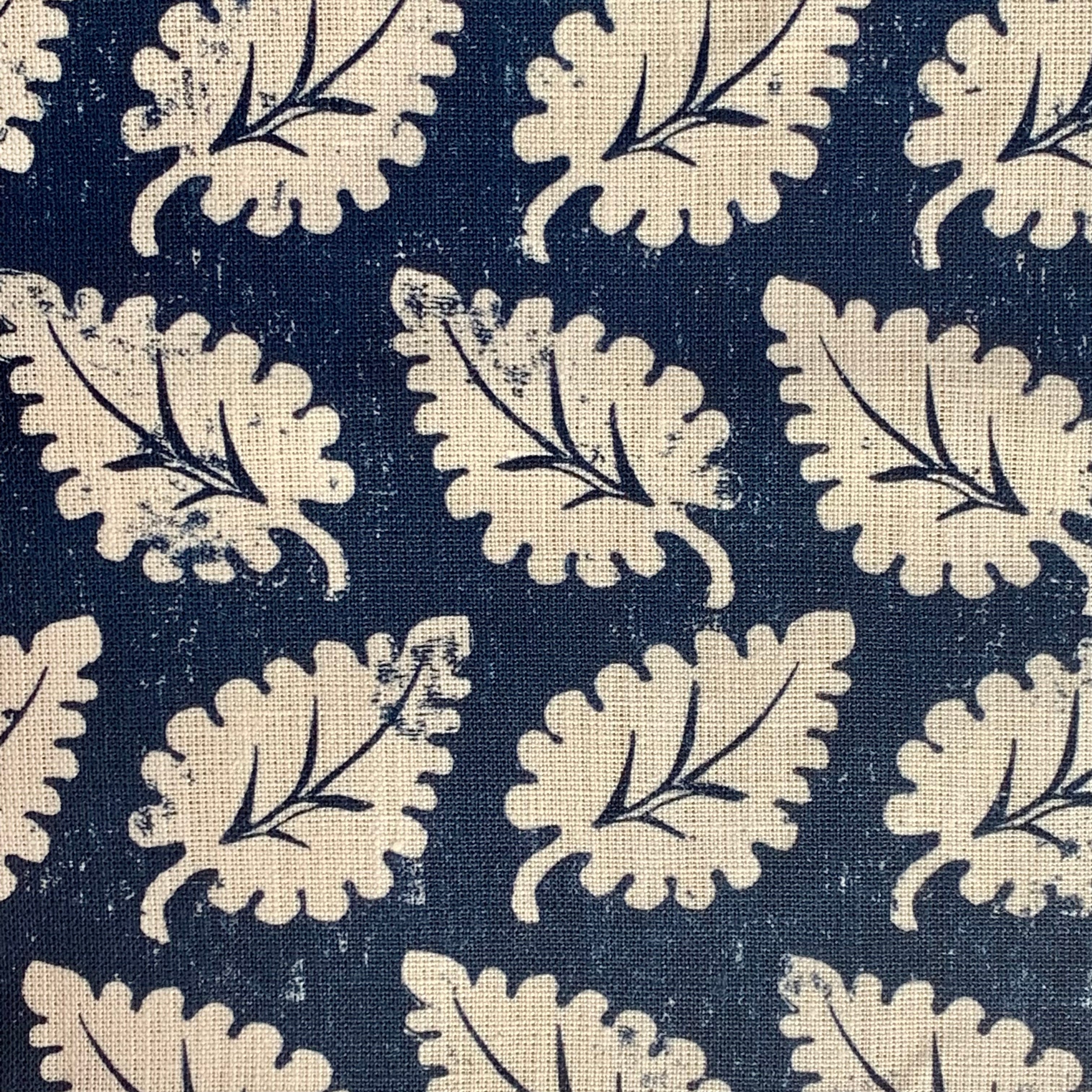 Detail of fabric in a repeating leaf print in cream on a navy field.