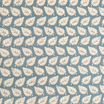 Detail of fabric in a repeating leaf print in cream on a blue field.