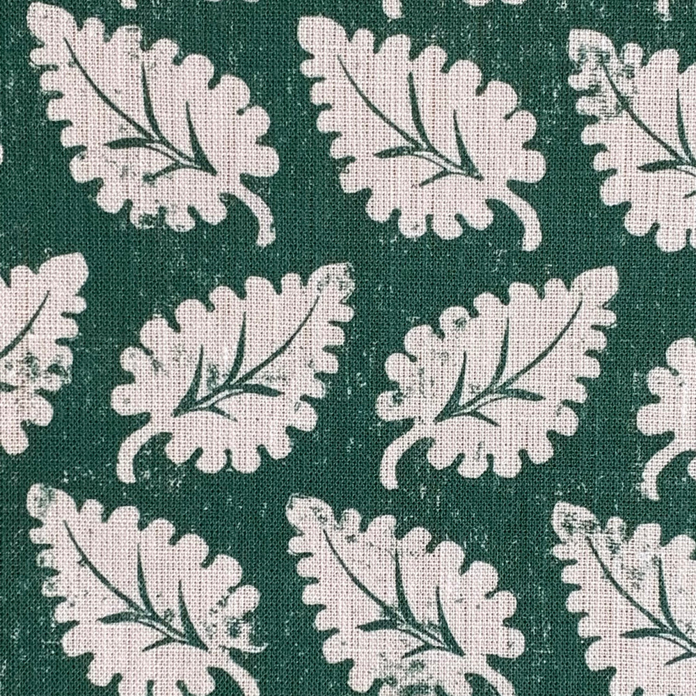 Detail of fabric in a repeating leaf print in white on a forest green field.