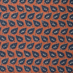 Detail of fabric in a repeating leaf print in navy and white on a rust field.