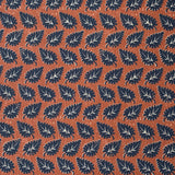 Detail of fabric in a repeating leaf print in navy and white on a rust field.