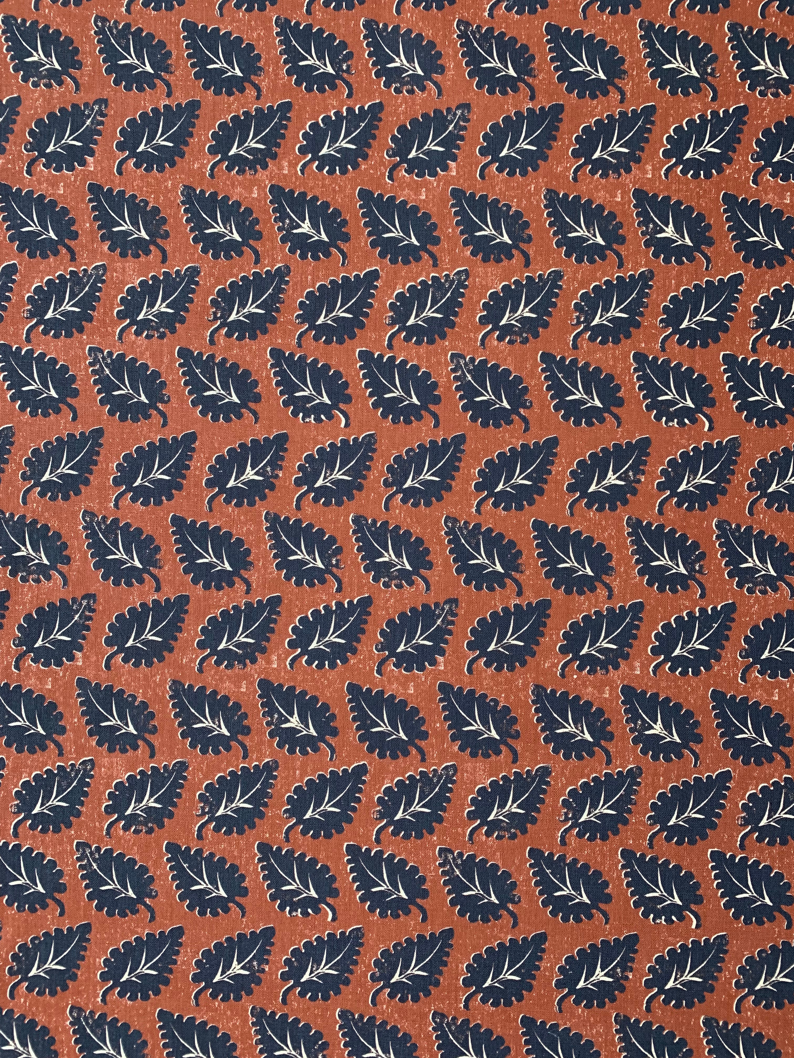 Detail of fabric in a repeating leaf print in navy and white on a rust field.