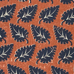 Detail of fabric in a repeating leaf print in navy and white on a rust field.