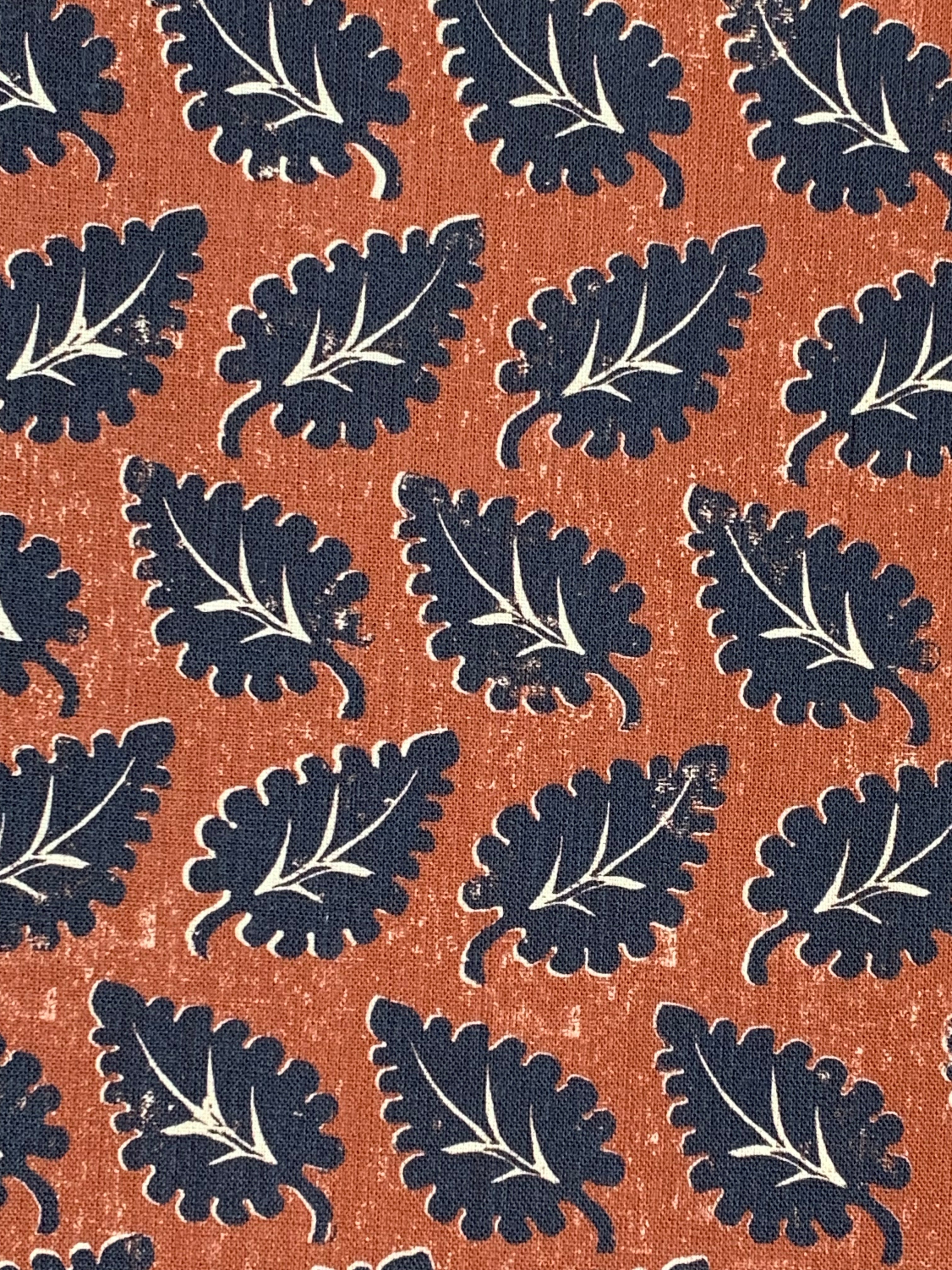 Detail of fabric in a repeating leaf print in navy and white on a rust field.