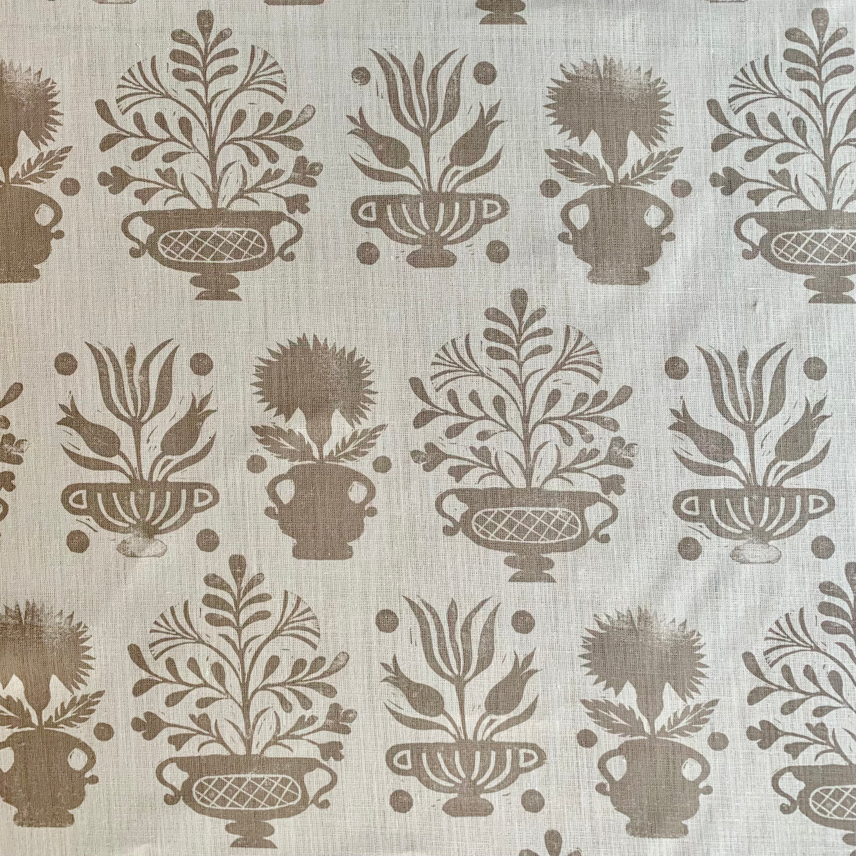 Detail of fabric in a repeating vase and plant print in tan on a white field.