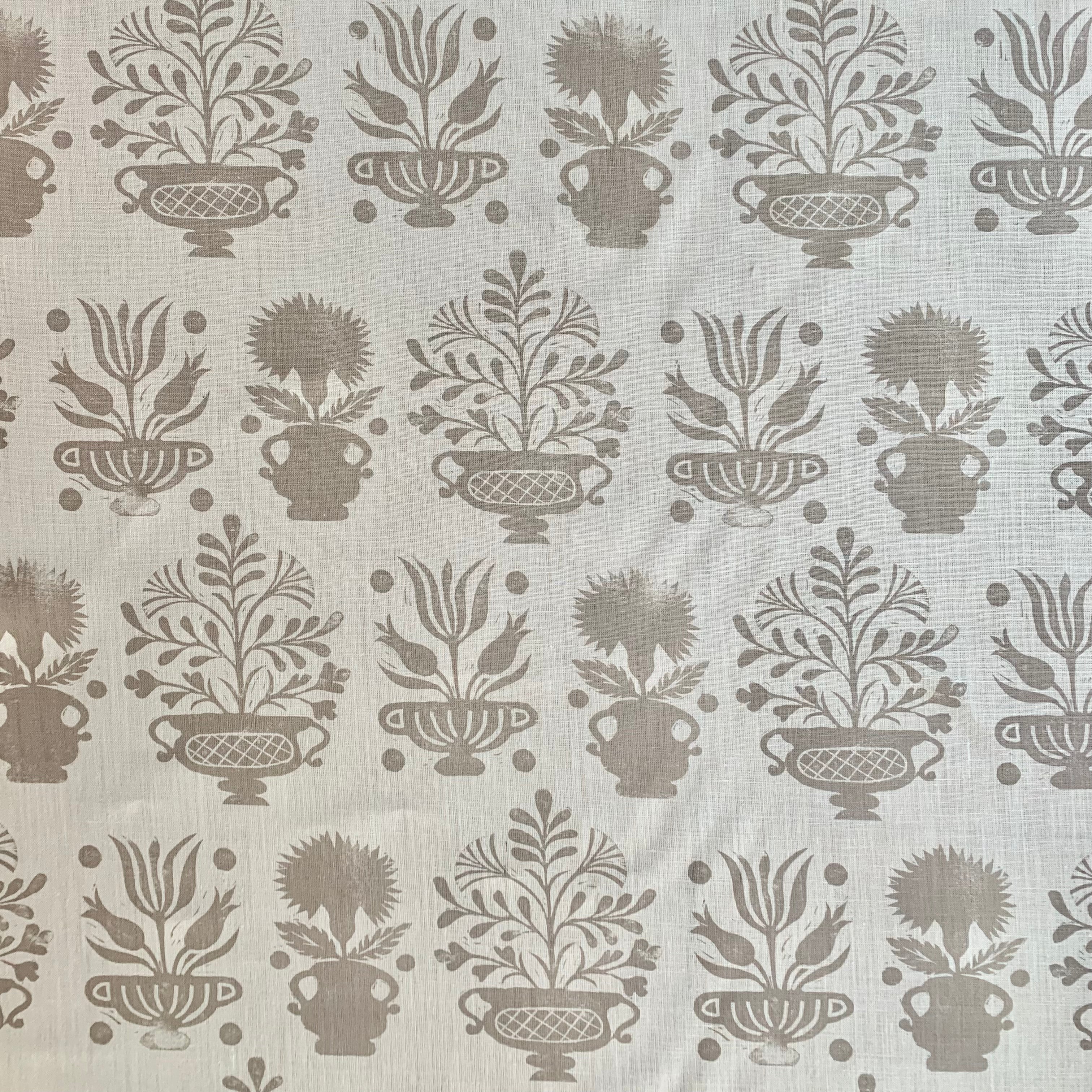 Detail of fabric in a repeating vase and plant print in tan on a white field.