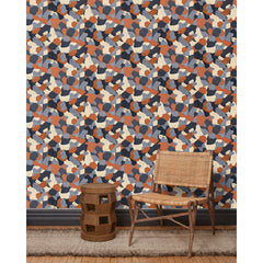 A wooden chair and end table in front of a wall papered in a painterly geometric pattern in shades of blue, cream and rust.