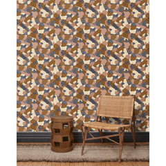 A wooden chair and end table in front of a wall papered in a painterly geometric pattern in shades of mauve, brown, cream and navy.