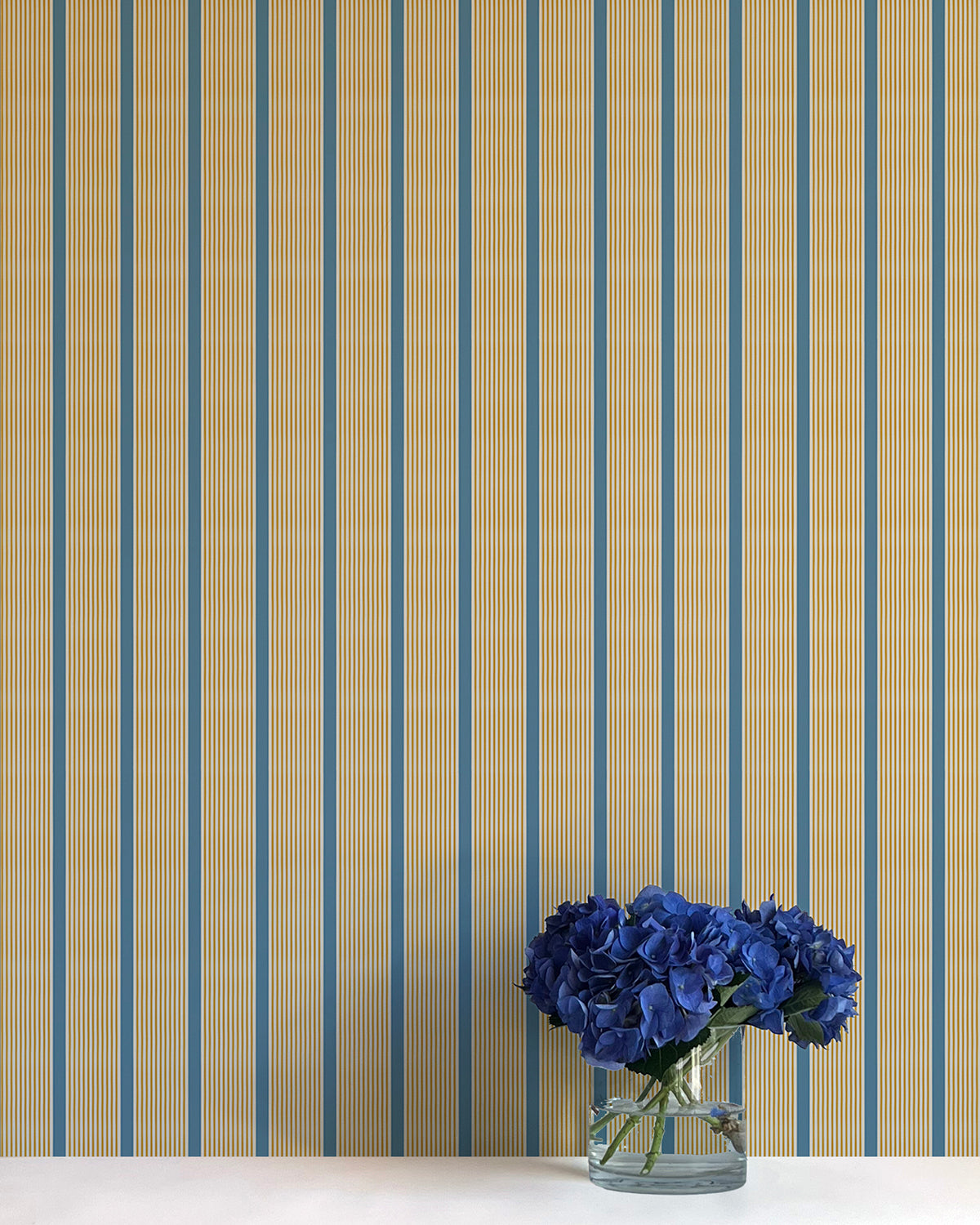 Striped wallpaper with a vase of blue flowers on a white surface