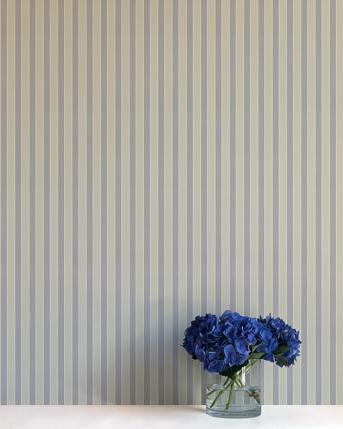 Striped wallpaper with a vase of blue flowers in the foreground