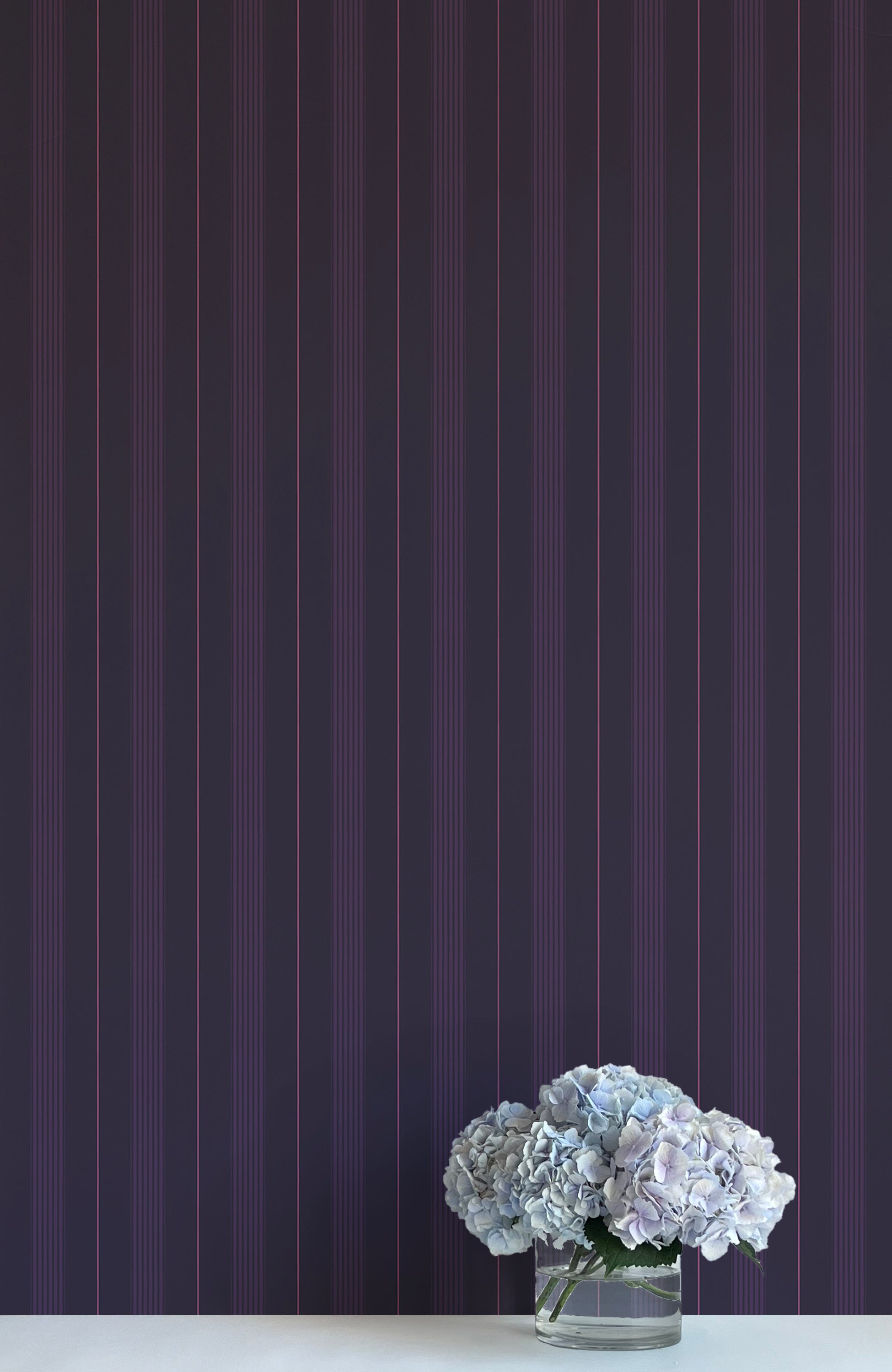 Vase of flowers on a white surface with a dark purple striped wallpaper background