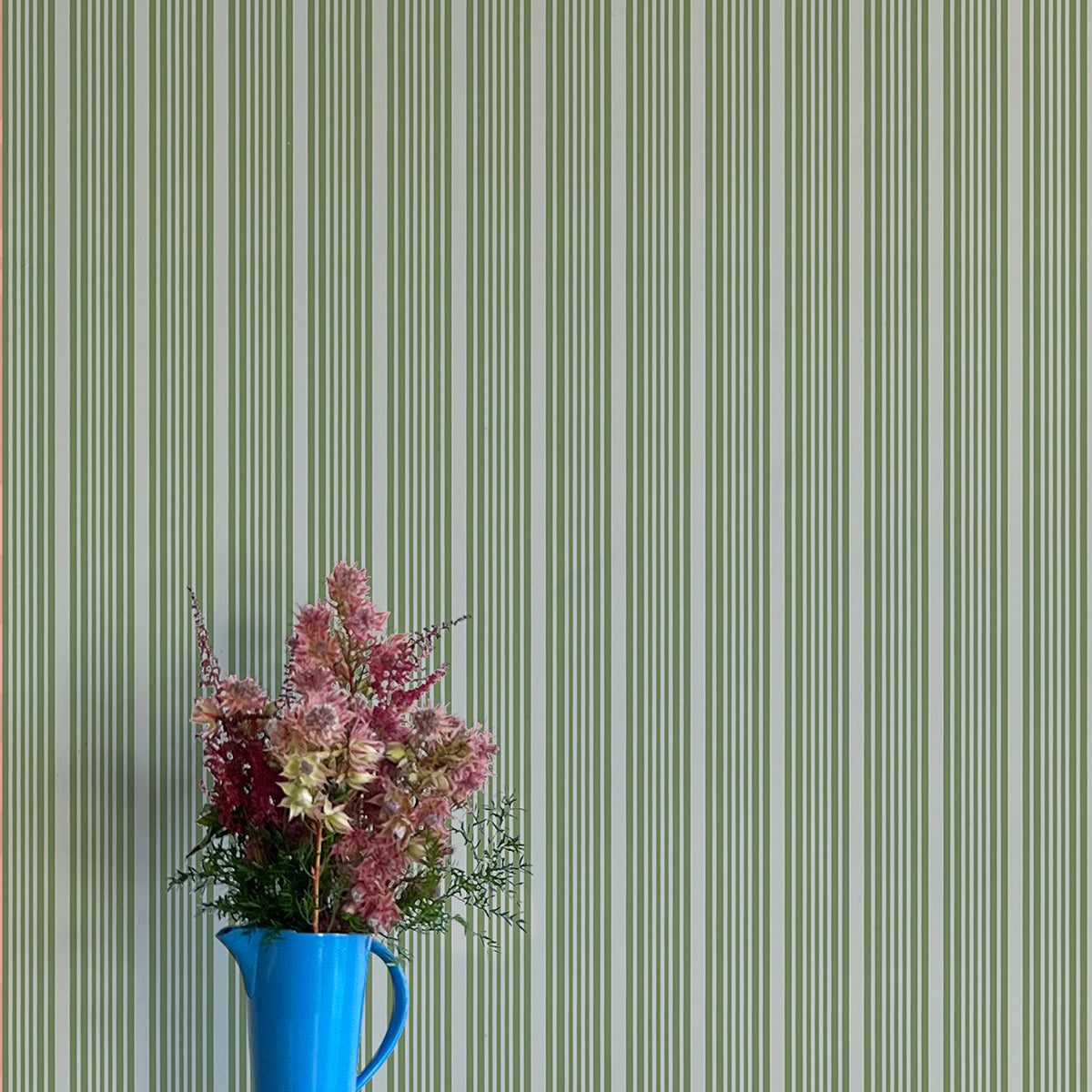 Blue pitcher with flowers against a green striped wallpaper background
