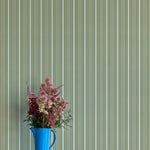 Blue pitcher with flowers against a green striped wallpaper background