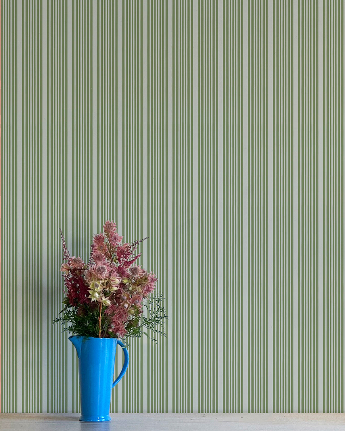 Blue pitcher with flowers against a green striped wallpaper background