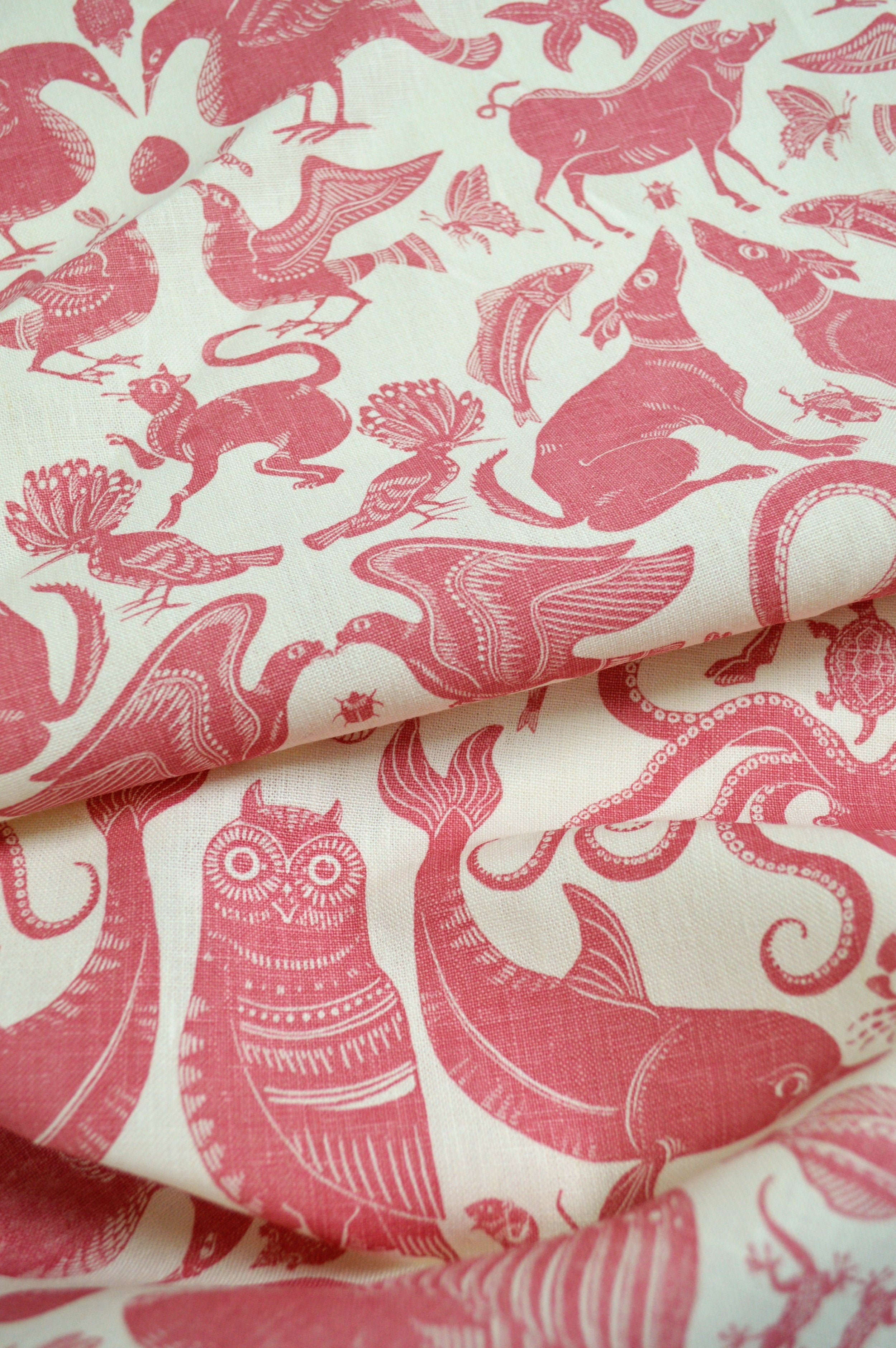 Draped patterned fabric with animals and sea creatures in pink on a white background