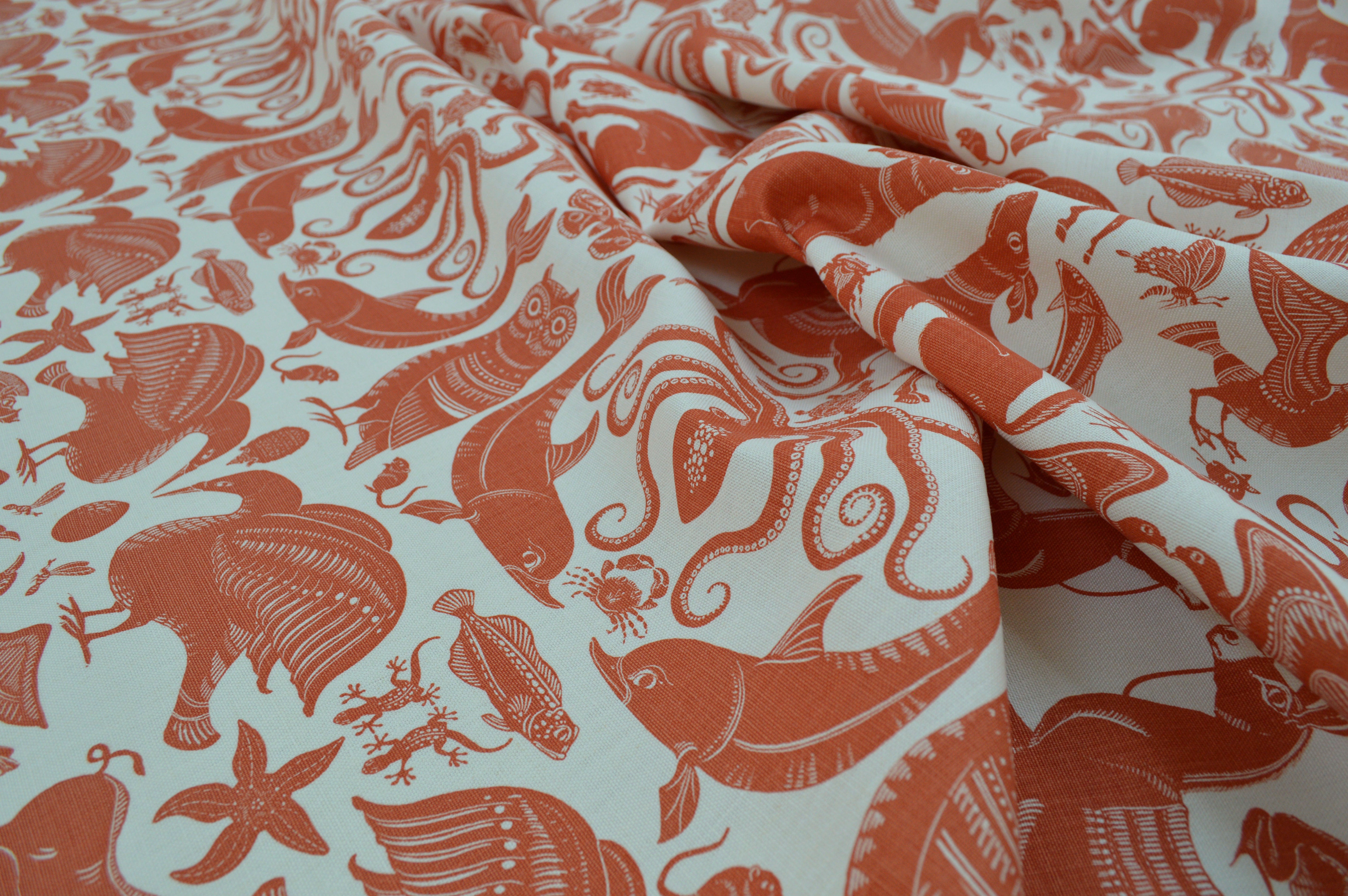 Draped patterned fabric with animals and sea creatures in orange on a white background